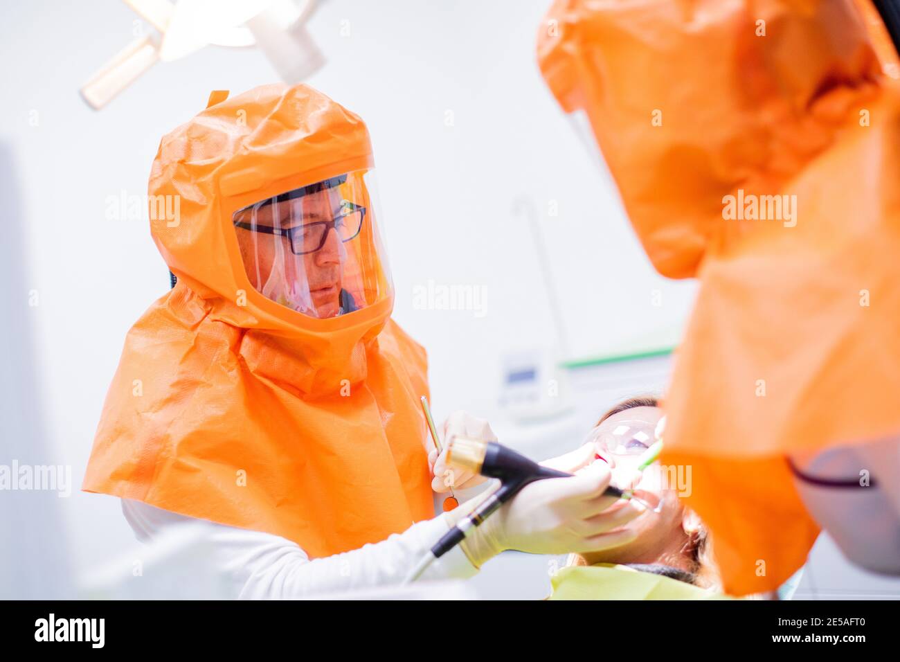 Oberhausen, Germania. 27 gennaio 2021. Ilker Sentürk (l), dentista, e Sultan Ekmen, assistente dentale in formazione, trattano un paziente in una sala di trattamento della sua pratica dentale presso il municipio, indossando cappe protettive complete. Sentürk vuole proteggere i suoi pazienti, il suo staff e se stesso dal coronavirus con le cappe protettive. Questi sono dotati di un sistema di filtro FFP3, che si trova su una cinghia e utilizza batterie ricaricabili per alimentare l'aria filtrata direttamente nel cofano tramite un tubo flessibile. Credit: Rolf Vennenbernd/dpa/Alamy Live News Foto Stock