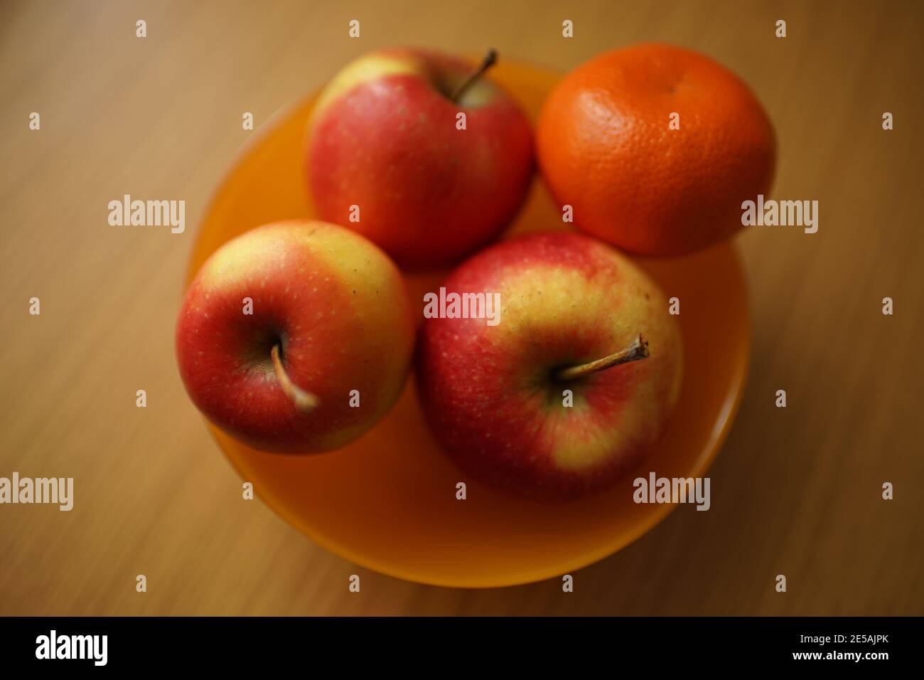 mandarino e tre mele rosse in piatto arancione sul tavolo di legno Foto Stock