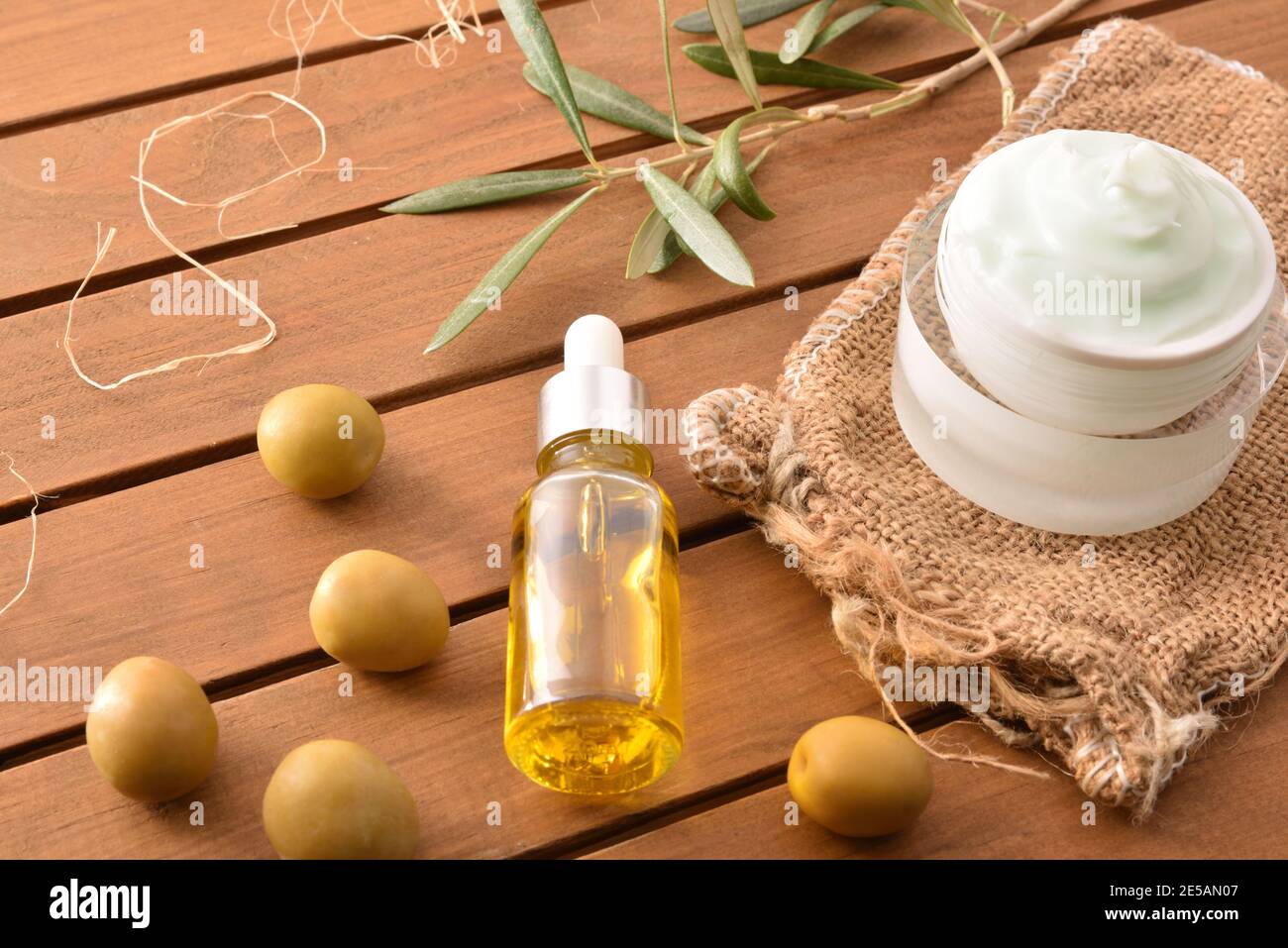 Crema naturale di pelle con estratto di oliva e siero con ramificazione e olive su tavola di legno. Vista dall'alto. Foto Stock