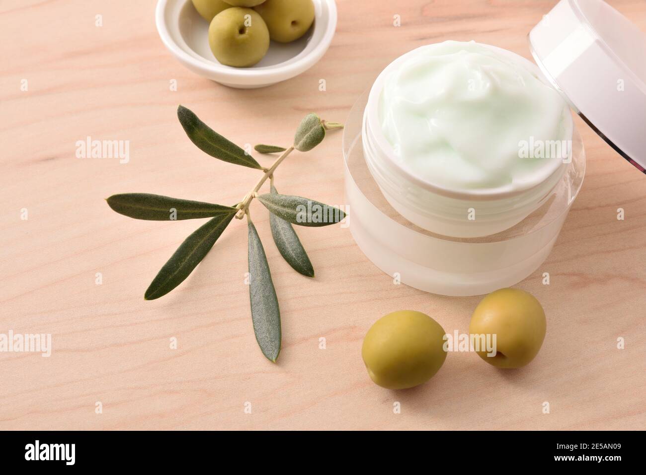 Crema cosmetica idratante con estratto di oliva per la pelle con rametto e olive su tavola di legno. Vista rialzata. Foto Stock