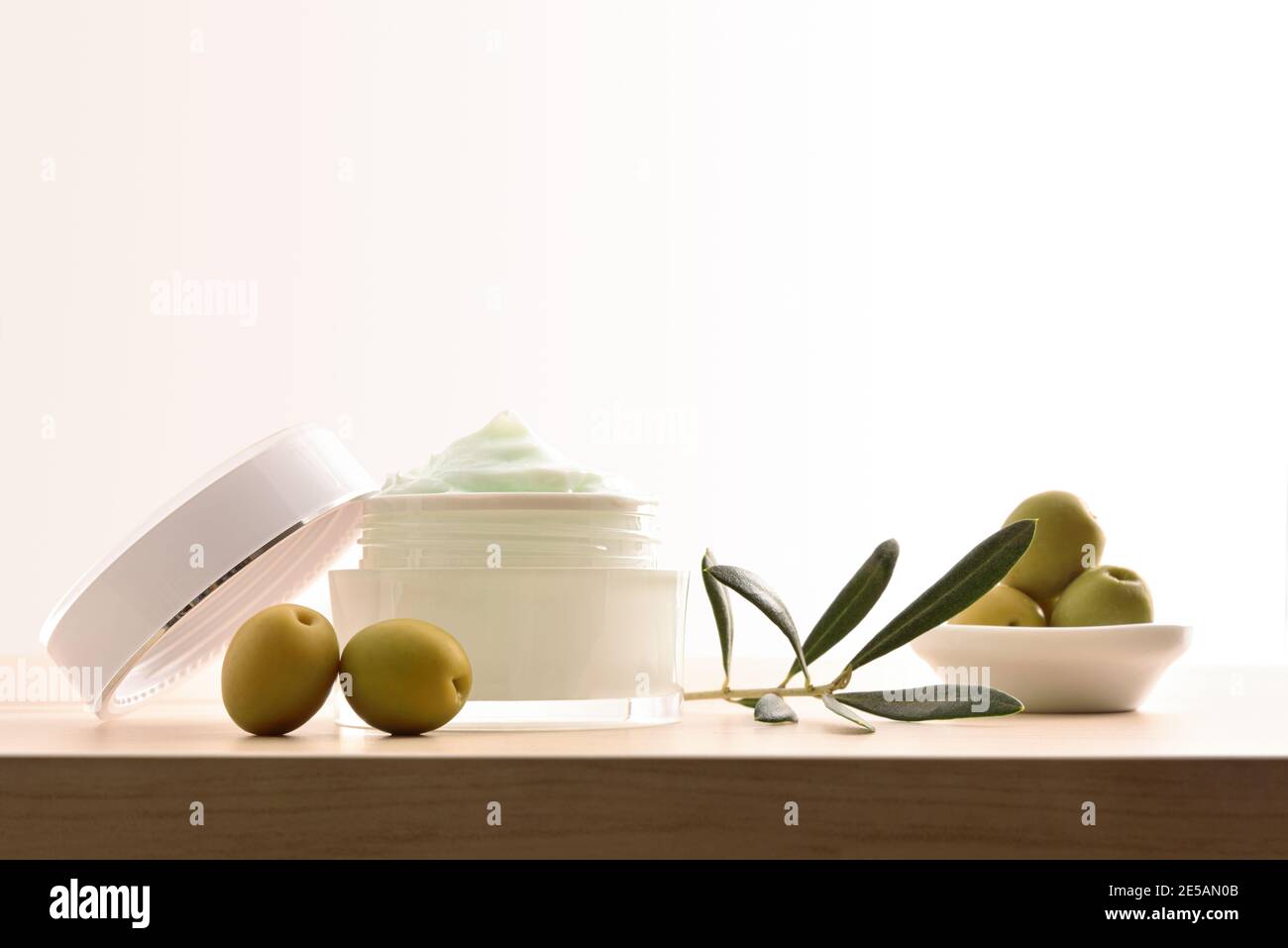 Crema cosmetica idratante con estratto di oliva per la pelle con rametto e olive su tavola di legno e fondo bianco isolato. Vista frontale. Foto Stock