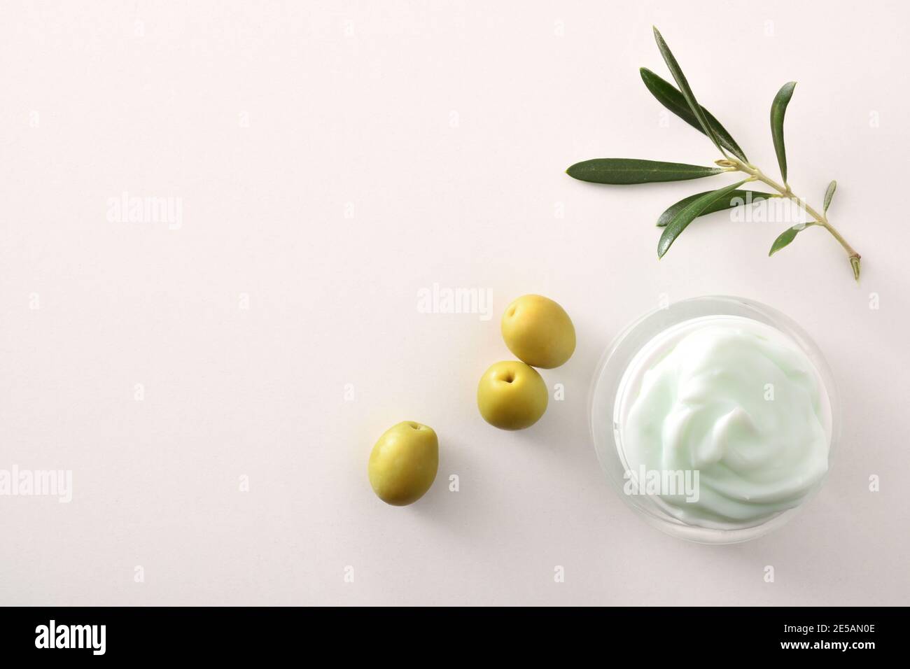 Crema cosmetica idratante con estratto di oliva per la pelle con rametto e olive su tavola bianca. Vista dall'alto. Foto Stock
