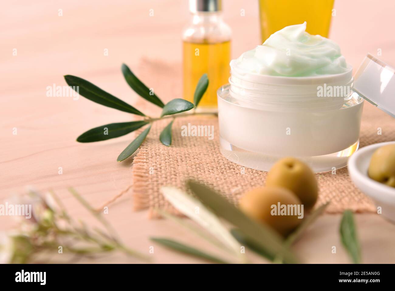 Crema cosmetica idratante con estratto di oliva per pelle e siero con rametto e olive su tavola di legno. Vista rialzata. Foto Stock
