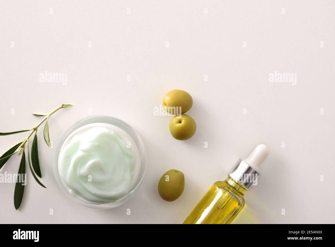 Crema cosmetica al siero e idratante con estratto di oliva per la pelle con rametto e olive su tavola bianca. Vista dall'alto. Foto Stock