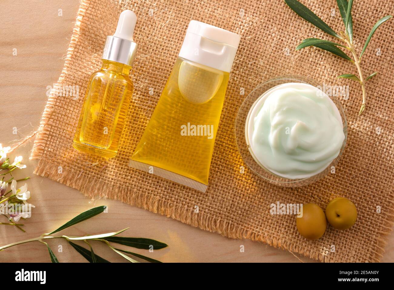 Olio di siero e crema cosmetica idratante con estratto di oliva per la pelle con rametto e olive su tavola di legno. Vista dall'alto. Foto Stock