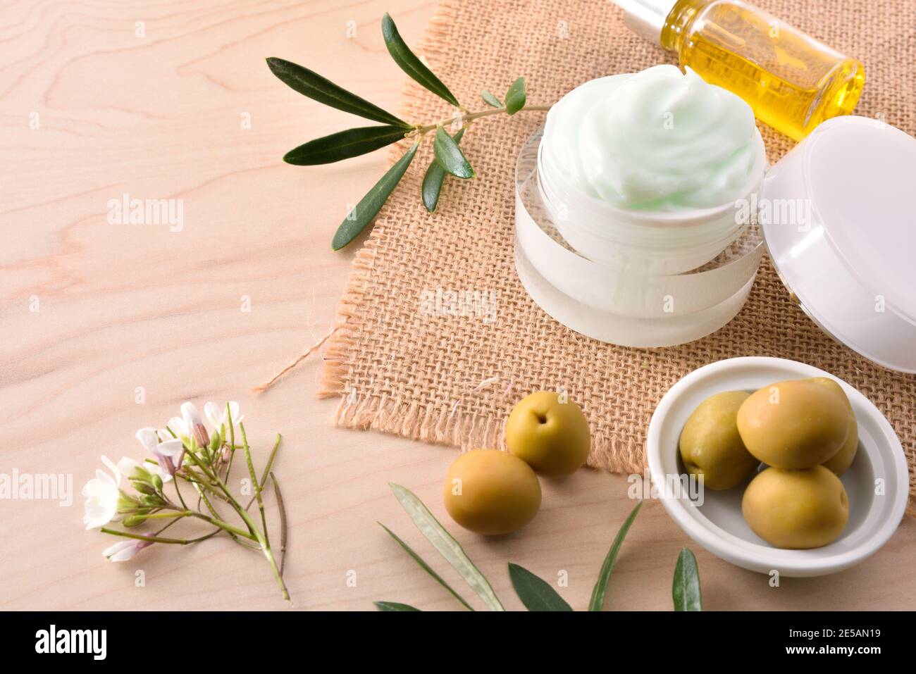 Crema idratante al siero e alle olive per la pelle su un piano di legno Foto Stock