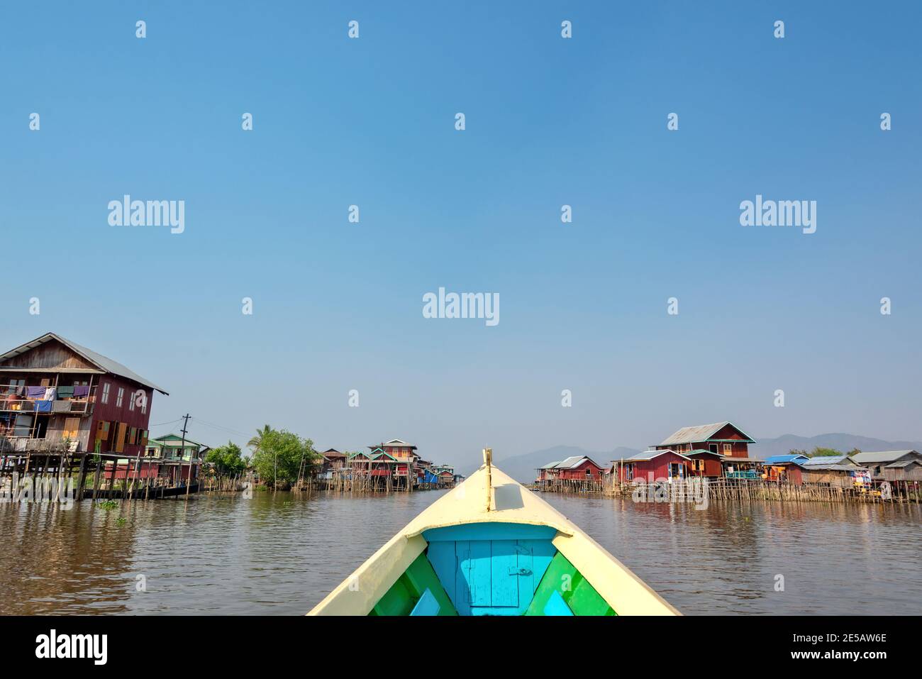 Barca che arriva in un colorato villaggio galleggiante con palafitte in Birmania, Myanmar Foto Stock