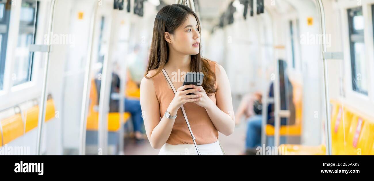 Giovane donna asiatica passeggero utilizzando smartphone e guardando fuori dal treno della metropolitana quando si viaggia in grande città, pendolari e trasporti co Foto Stock