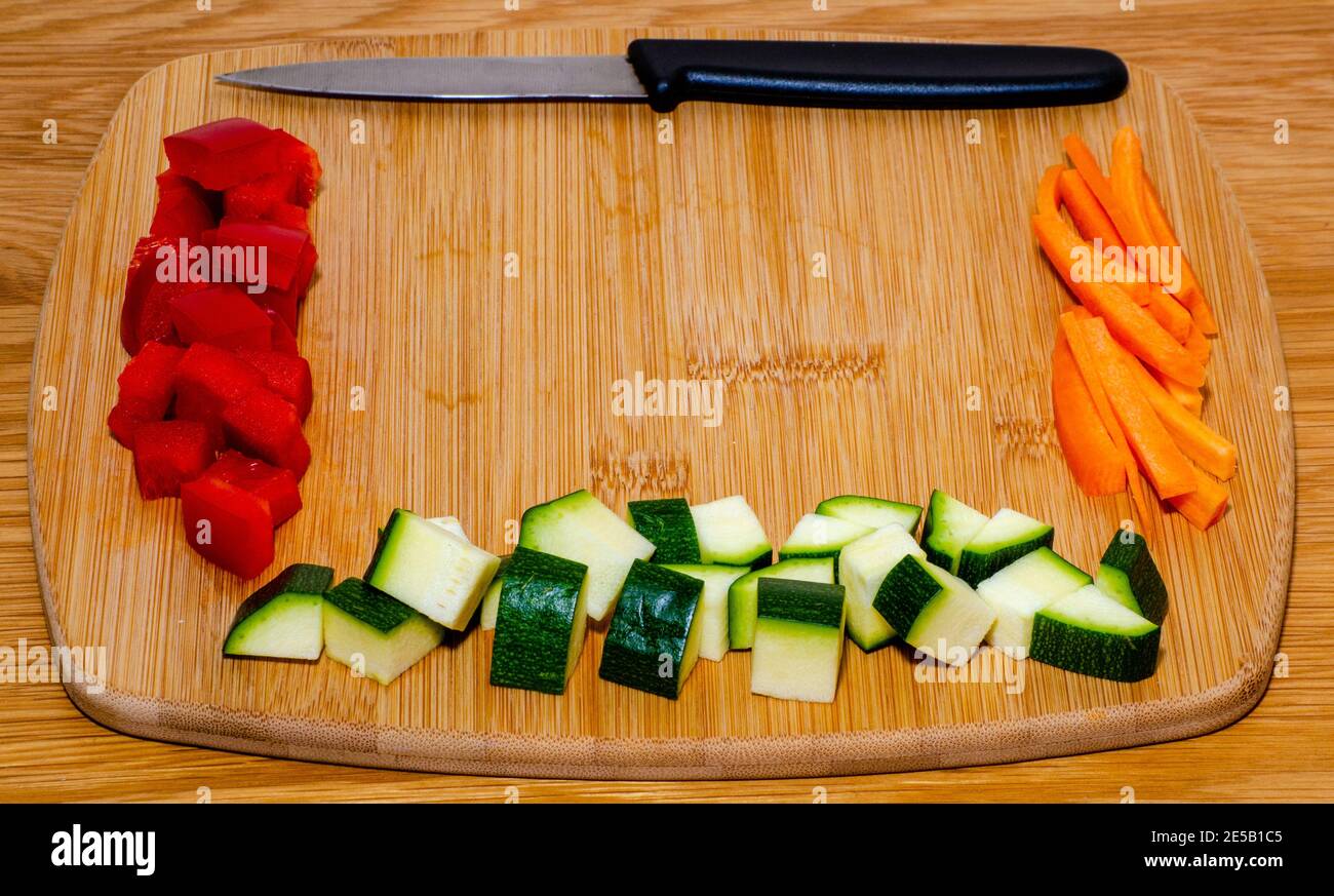 Pepe a dadini e zucchine con bastoncini di carote disposti su legno tagliere con coltello e sfondo in legno con messa a fuoco selettiva e spazio di copia Foto Stock