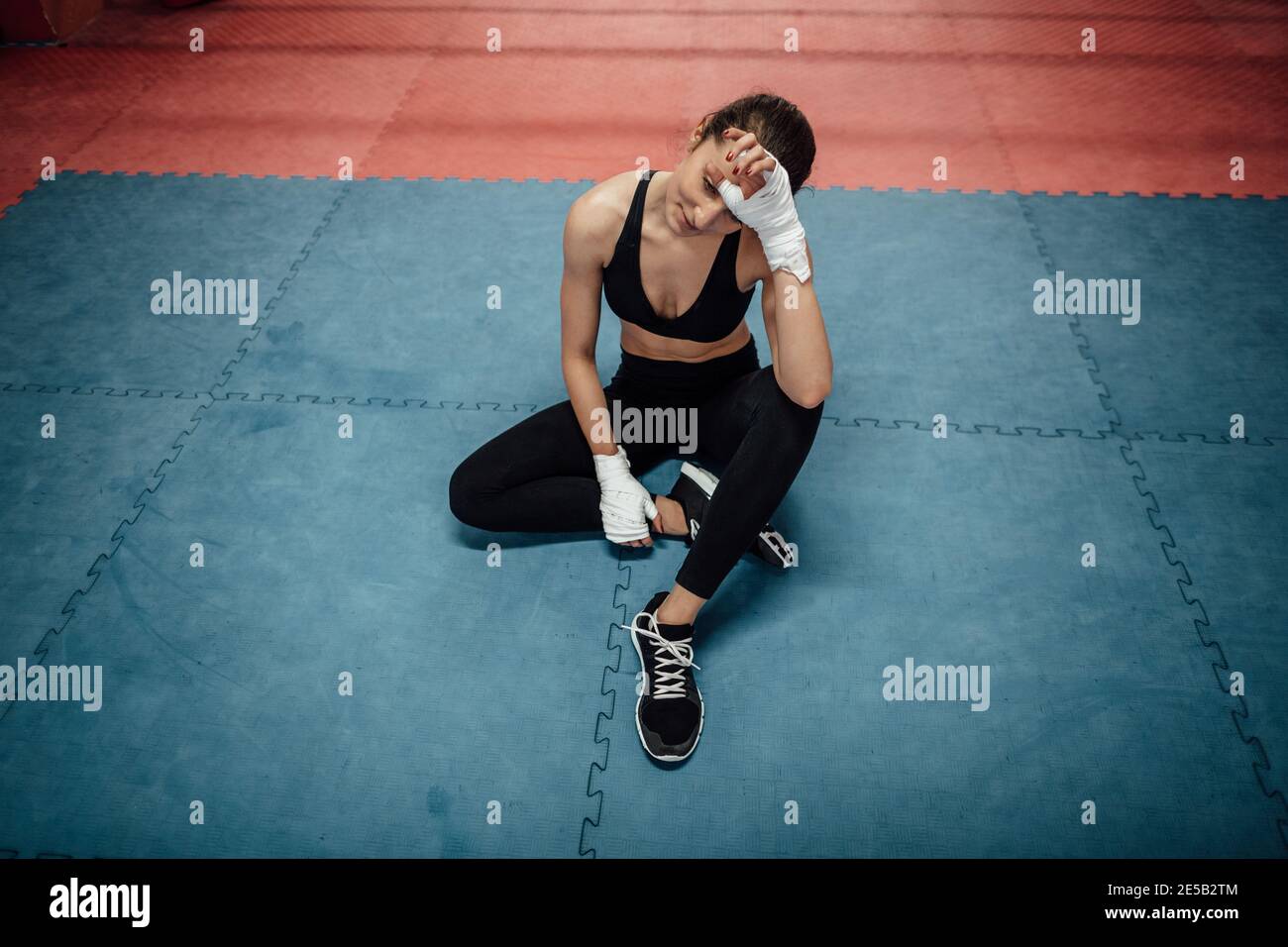 Un ritratto di una giovane atleta che si rilassa dopo un allenamento in palestra. Una sportiva esausta seduta su un tappetino e che prende una pausa dall'esercizio fisico. Foto Stock