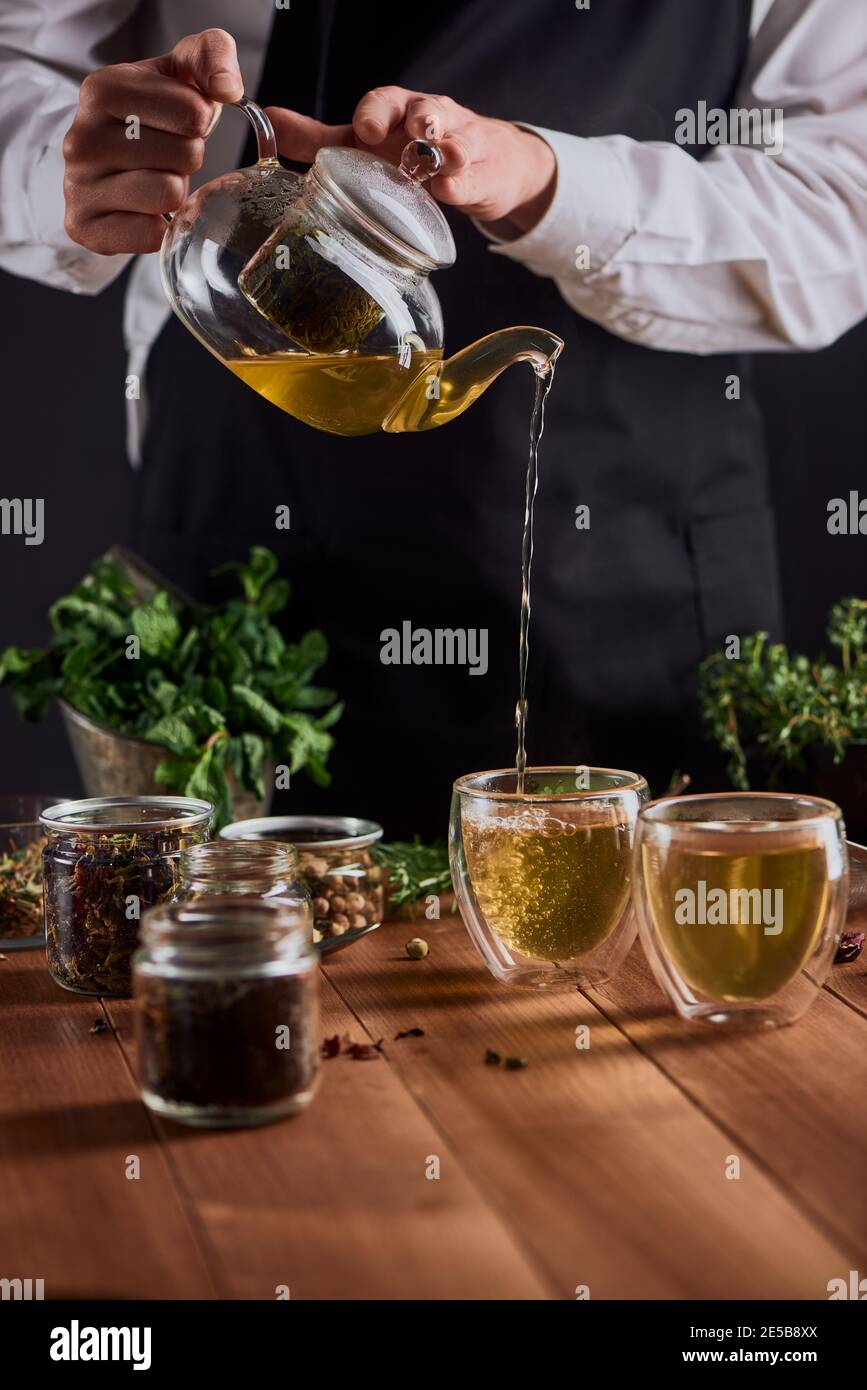 Barista che versa il tè alle erbe appena preparato in due tazze da una teiera Foto Stock