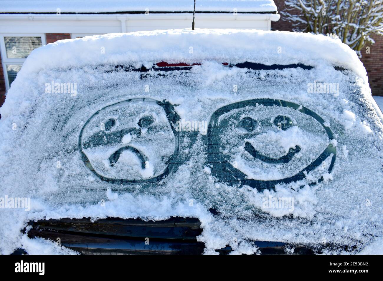 primo piano della schermata dell'auto coperta di neve con due volti emoji attratti dal ghiaccio, uno felice e uno triste. fuori in un freddo giorno di sole inverno Foto Stock