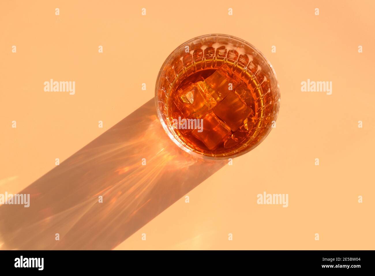 Bicchiere di whisky con cubetti di ghiaccio su sfondo beige e ombra soleggiata. Vista dall'alto Foto Stock