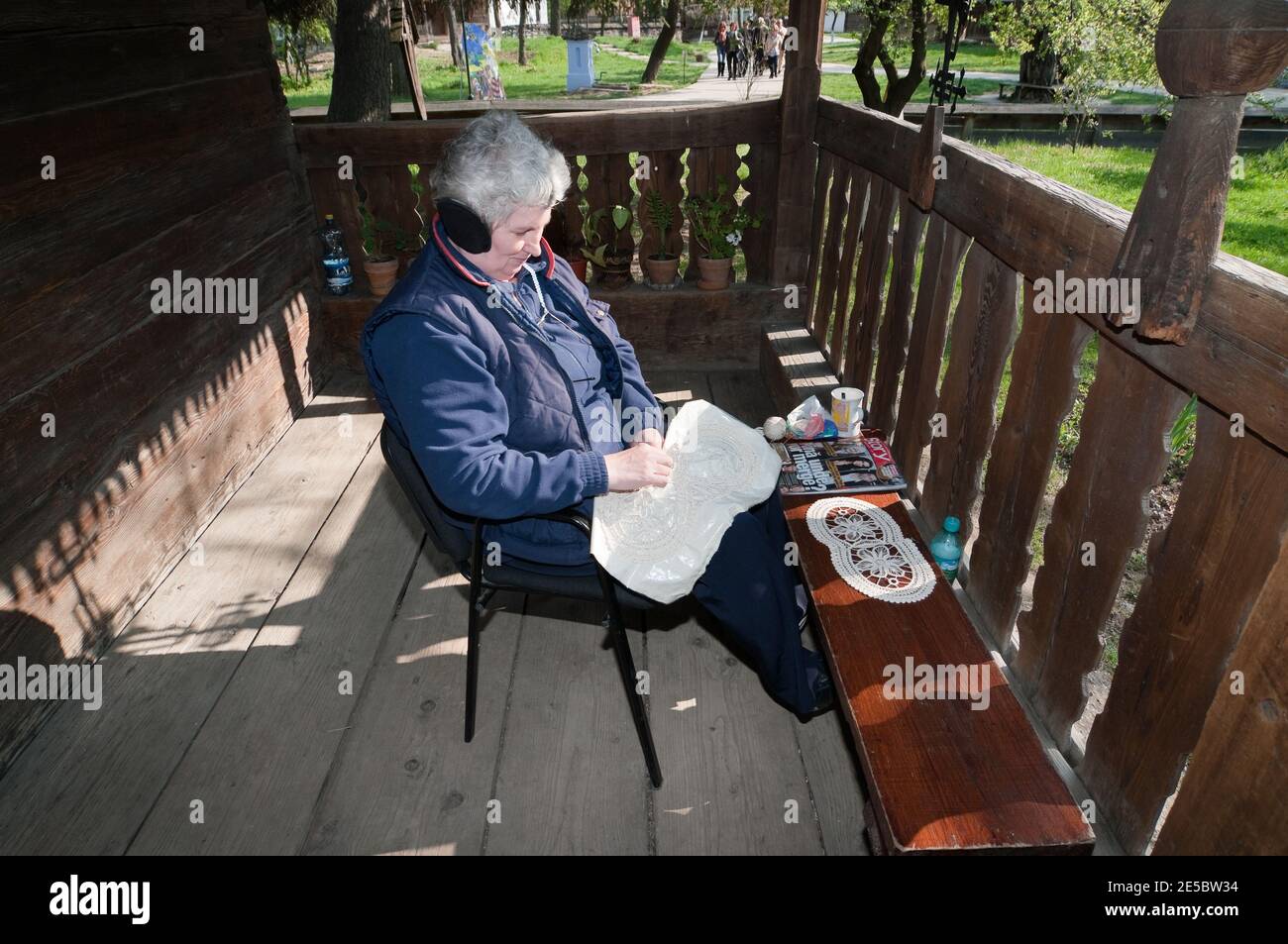 Donna ricamata sul portico anteriore di una casa in legno nel Museo del Villaggio di Bucarest, Romania Foto Stock