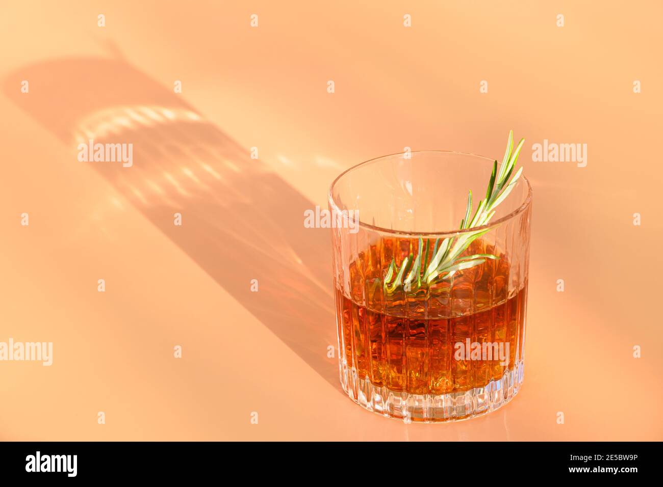Un bicchiere di whisky freddo guarnire il rosmarino su sfondo beige con un'ombra soleggiata. Foto Stock