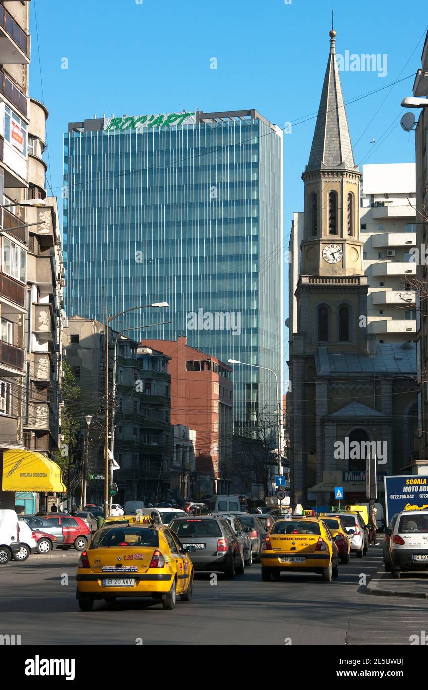 Bucarest, Romania - 21 aprile 2011: Contrasto per un nuovo grattacielo e un vecchio campanile, il traffico e taxi gialli in una via Bucarest, Romania Foto Stock