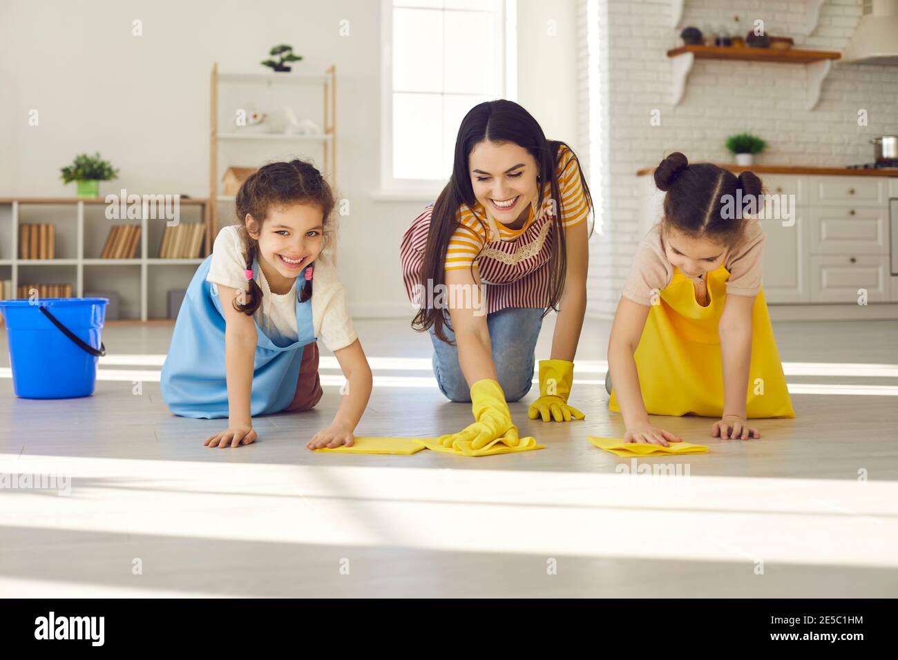 Una giovane e felice madre e le sue piccole figlie che si strofinano il pavimento insieme Foto Stock
