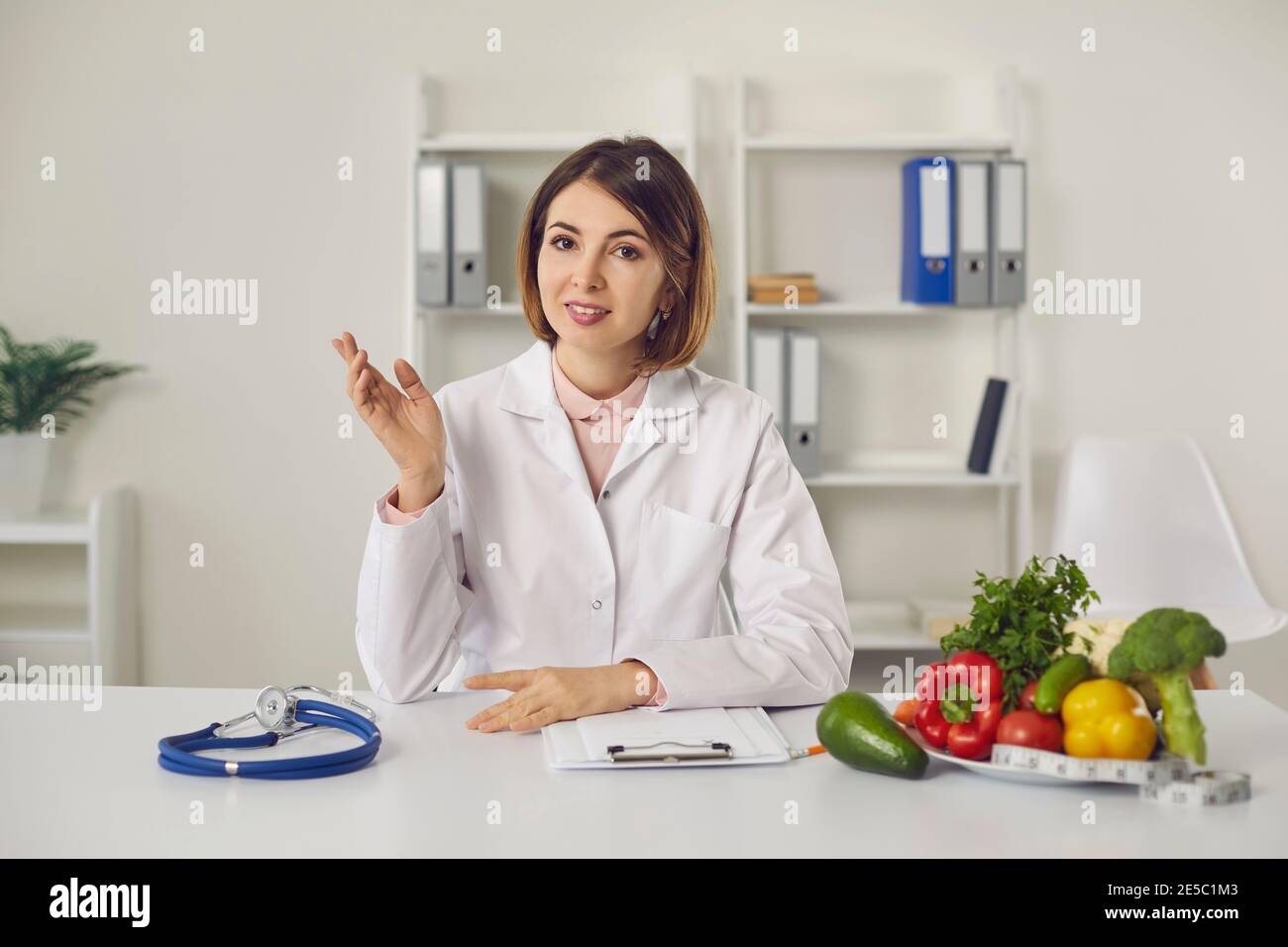 Nutrizionista seduto alla scrivania della clinica e raccontando benefici di una dieta sana Foto Stock