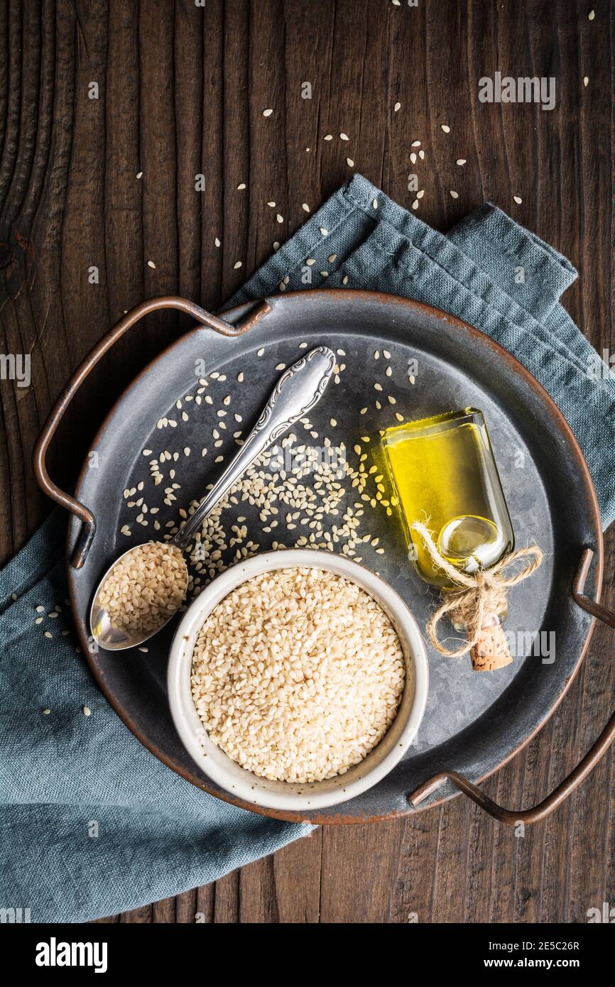 Olio di sesamo pressato freddo sano in una bottiglia di vetro e. semi in una ciotola su sfondo di legno Foto Stock