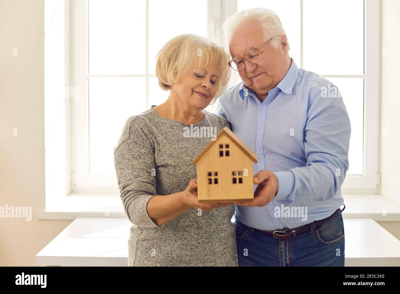 Sorridente coppia anziana guardando un modello di legno di una casa che viene tenuta nelle loro mani. Foto Stock
