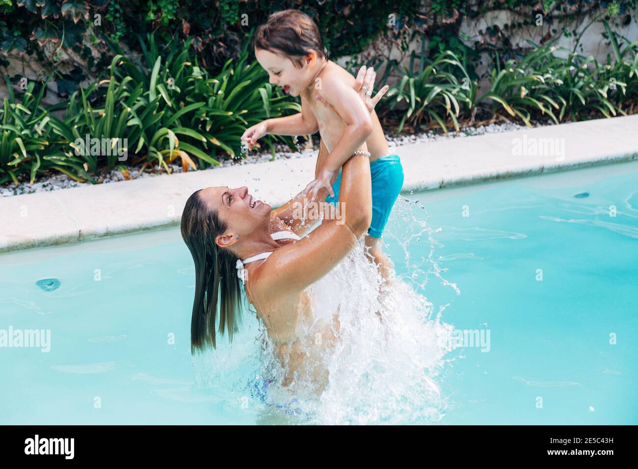 Mamma un figlio che gioca in acqua in una piscina. Il bambino felice è gettato in su da sua madre. Stile di vita. Foto Stock