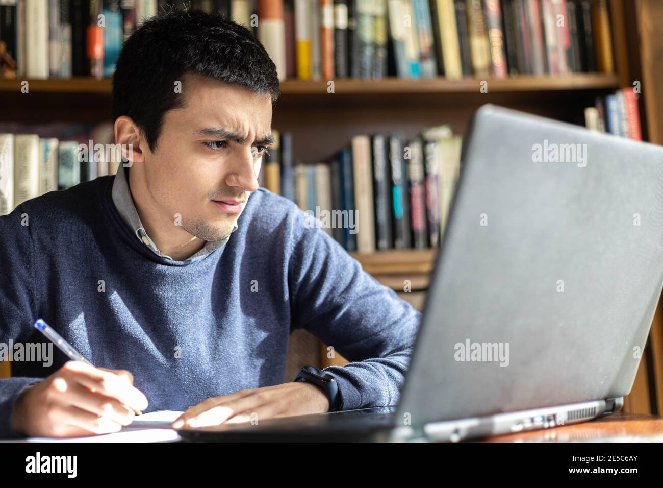 fuoco selettivo di un giovane sorpreso dalle note ha sul computer mentre lavora o studia online e prendere appunti in un notebook su cui è posizionato Foto Stock
