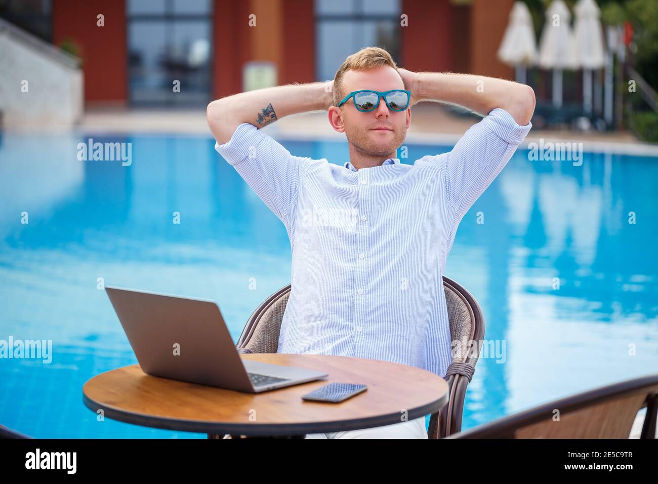 Uomo d'affari di successo bello maschio in occhiali da sole lavora ad un  computer portatile seduto vicino alla piscina. Lavoro remoto. Freelance  Foto stock - Alamy