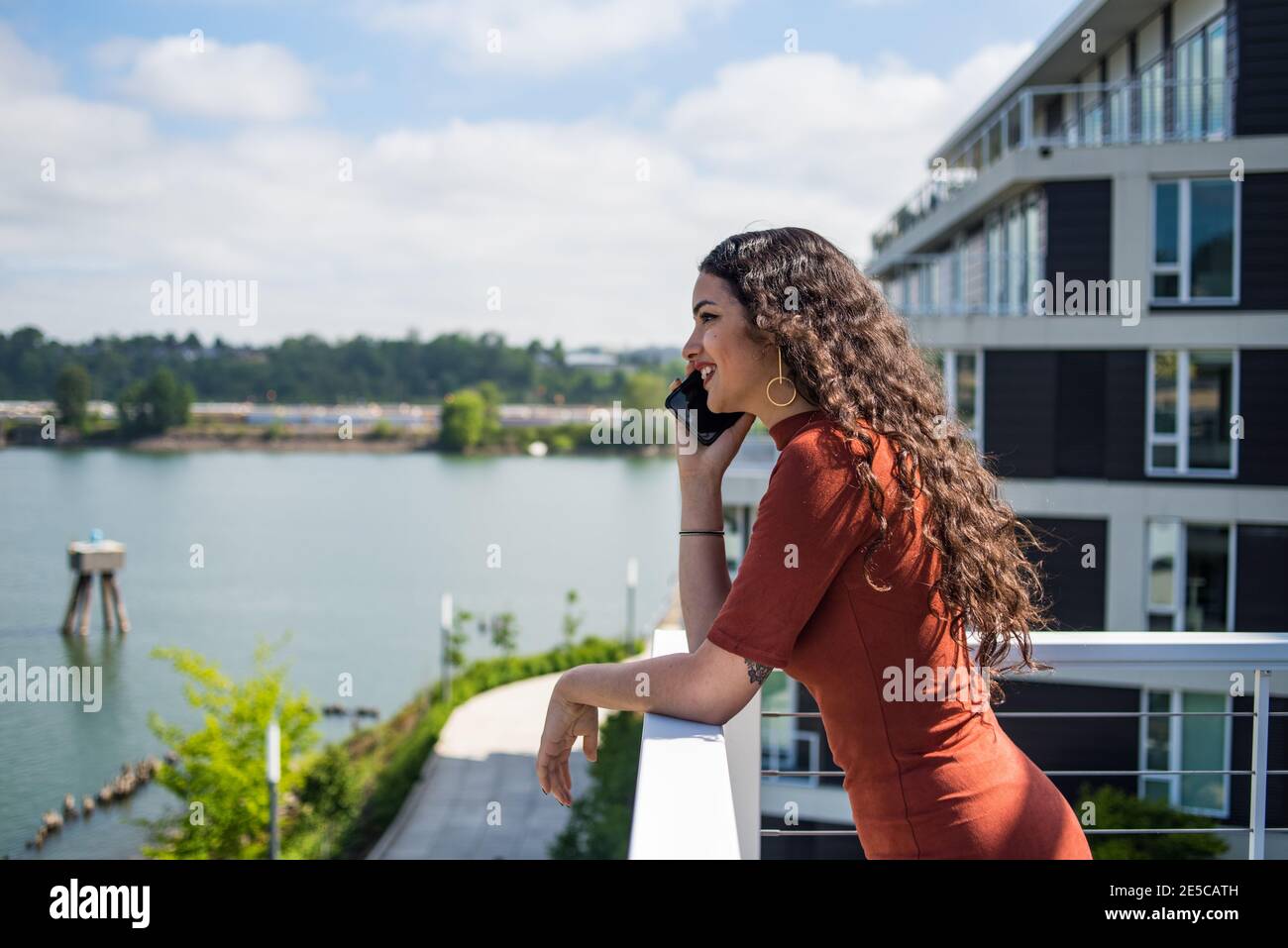 Felice giovane donna che parla al telefono sul balcone della città con fiume Foto Stock