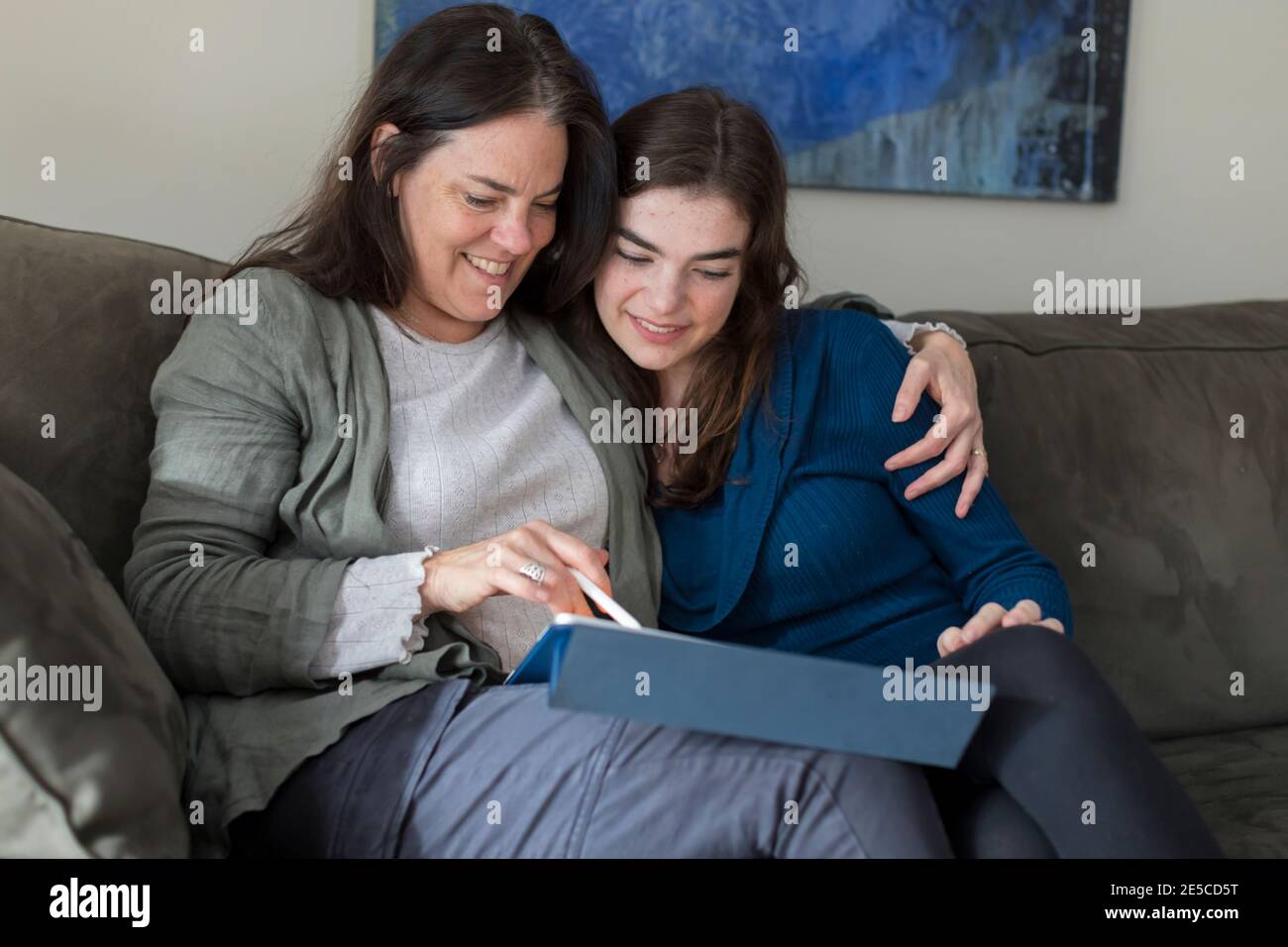 Madre con braccio intorno a teen figlia sorridente e guardando tablet Foto Stock