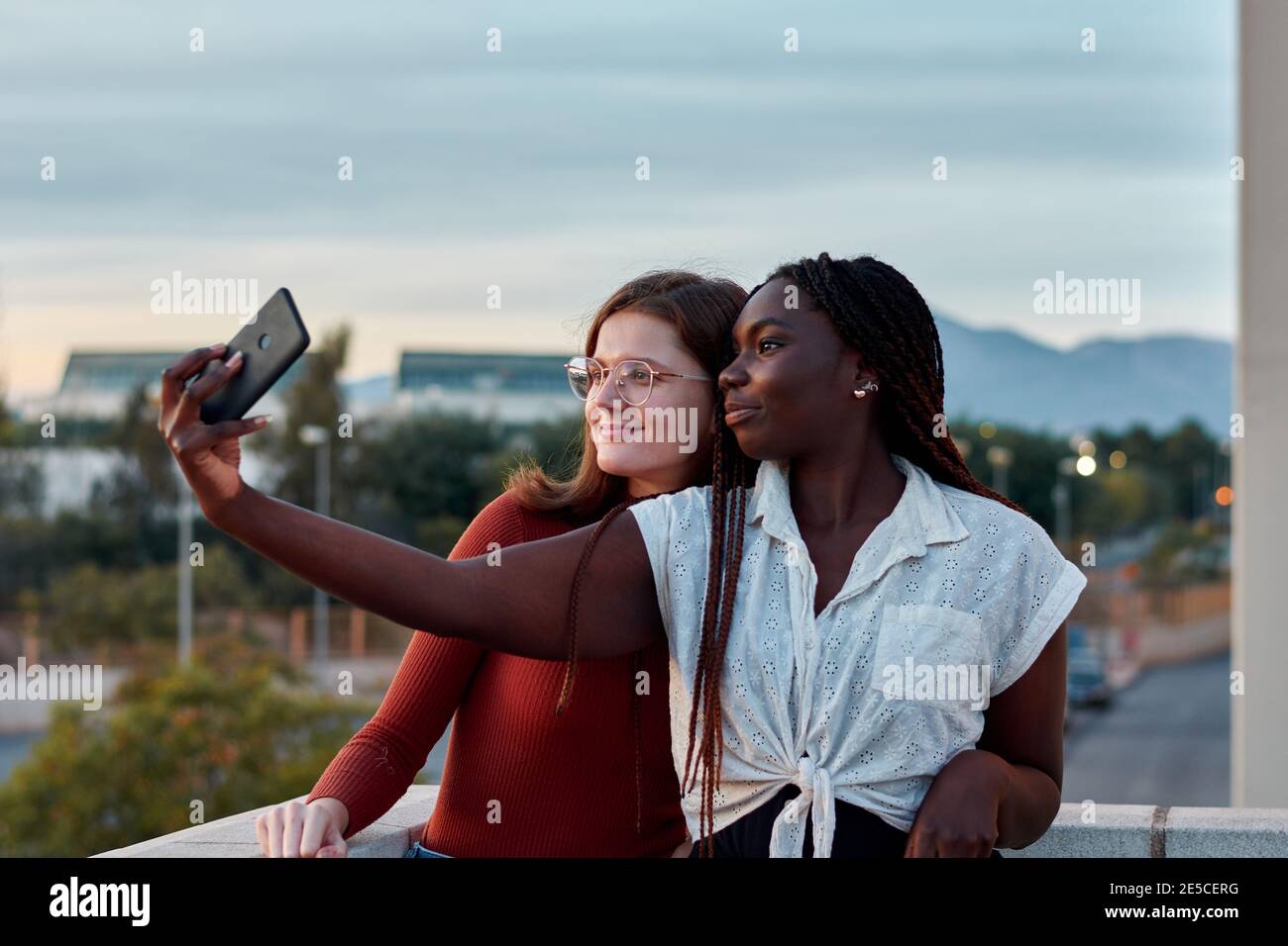 Due giovani donne stanno prendendo un auto-ritratto con il loro telefono al tramonto Foto Stock