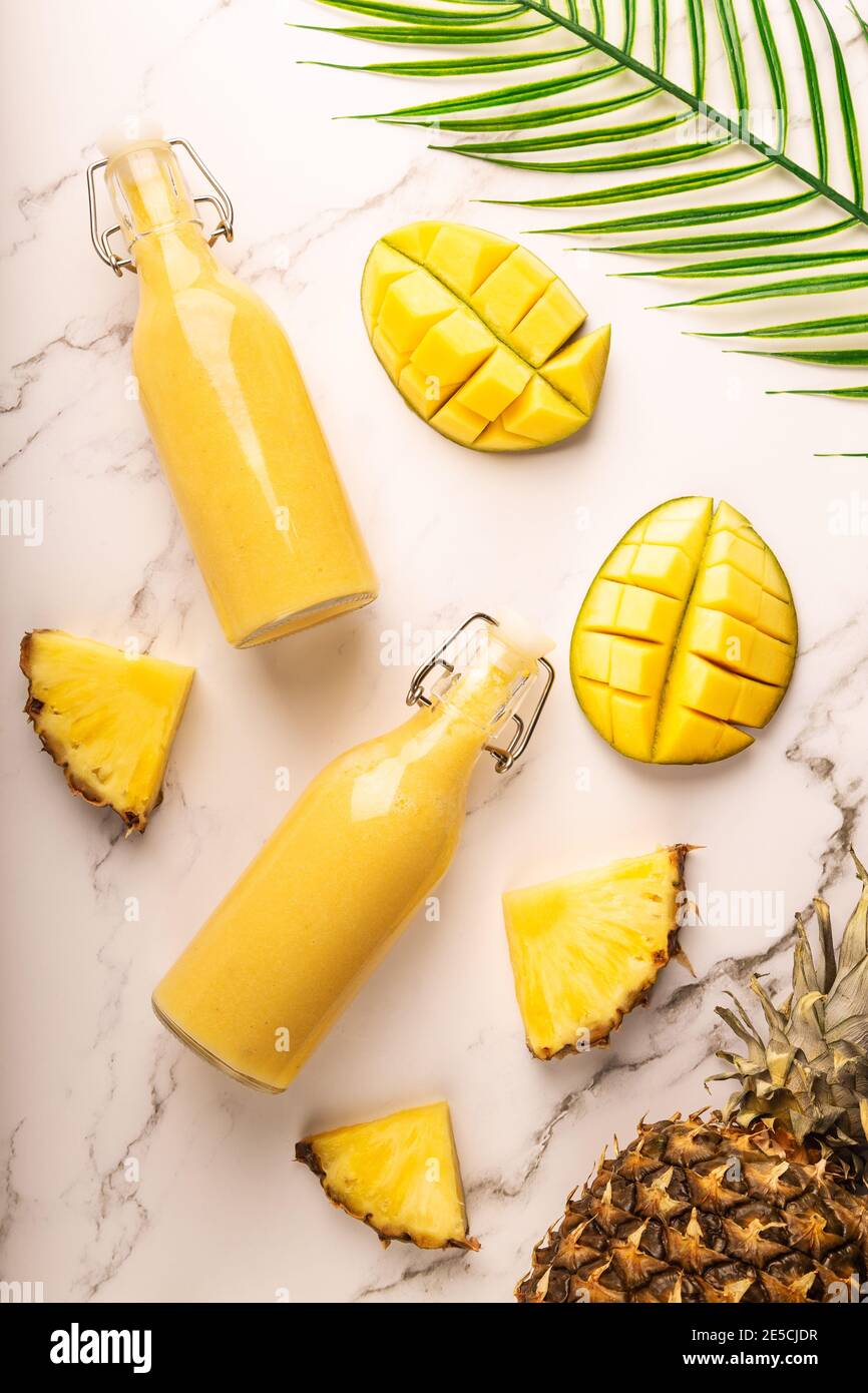 Frullato tropicale fresco con ananas e mango in bottiglie su sfondo marmoreo. Vista dall'alto. Foto Stock