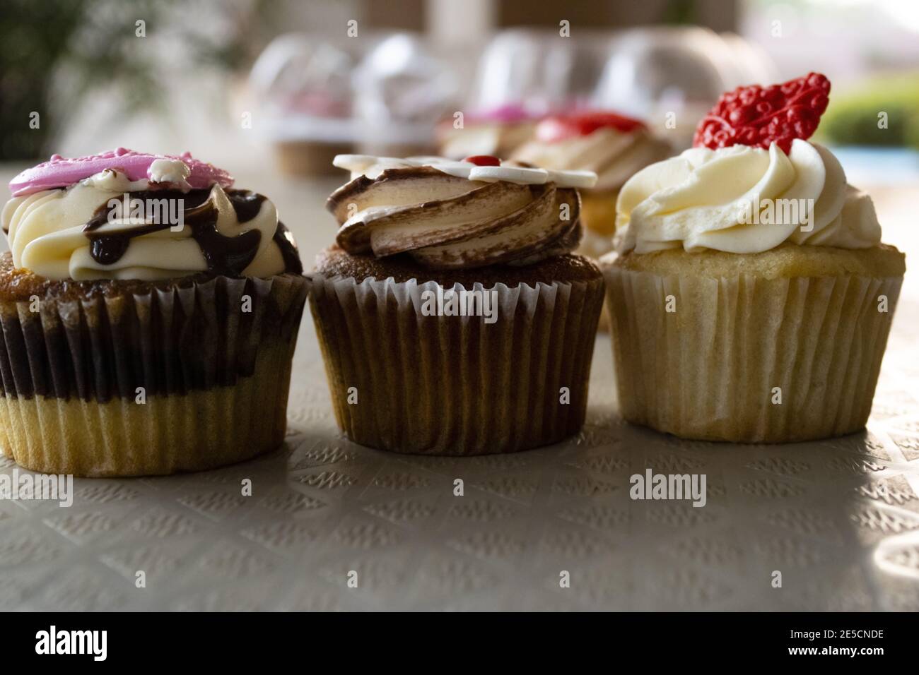 Primo piano di cupcake in marmo con salsa al cioccolato, cupcake al butterscotch con glassa e cupcake alla vaniglia con crema al burro, con fondati di dessert Foto Stock