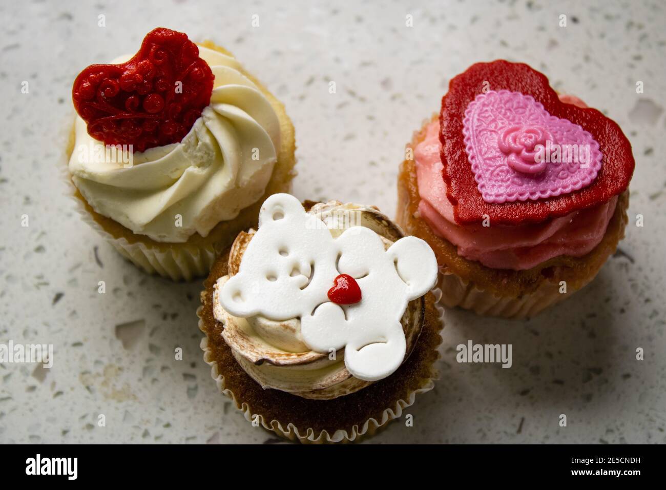 Primo piano di cupcake di butterscotch con glassa di crema bianca e marrone con fondente di orsacchiotto bianco e cuore rosso per la giornata di San Valentino, con marmo Foto Stock