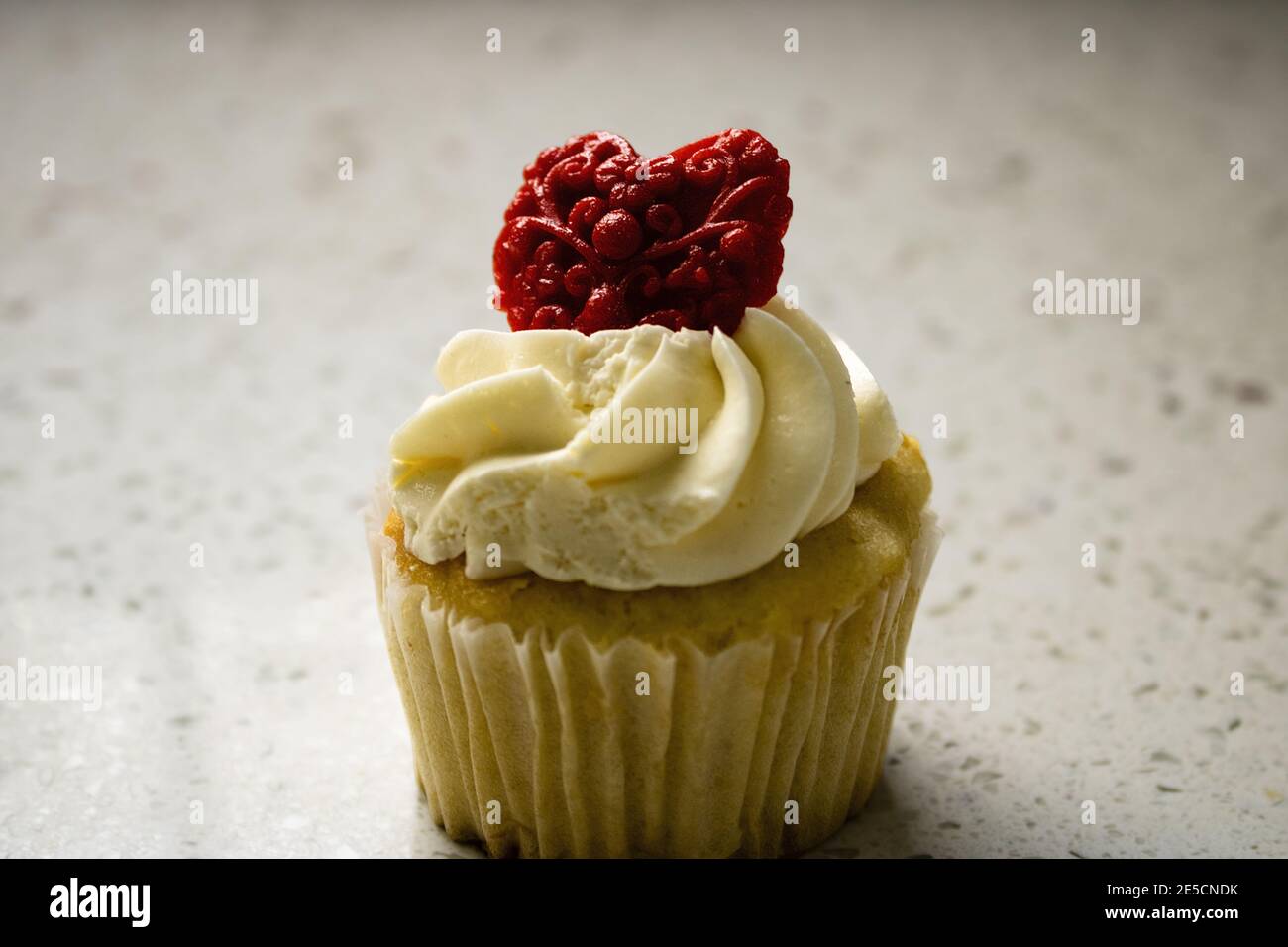 Primo piano di cupcake alla vaniglia con glassa di panna bianca cuore rosso fondente modellato per il giorno di san valentino Foto Stock