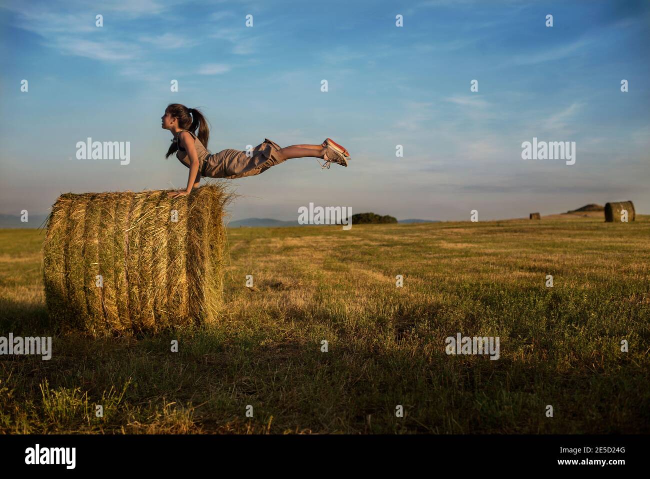 Una ragazza adolescente che si bilancia sulle sue mani a metà aria su una balla di fieno in un campo, Bulgaria Foto Stock