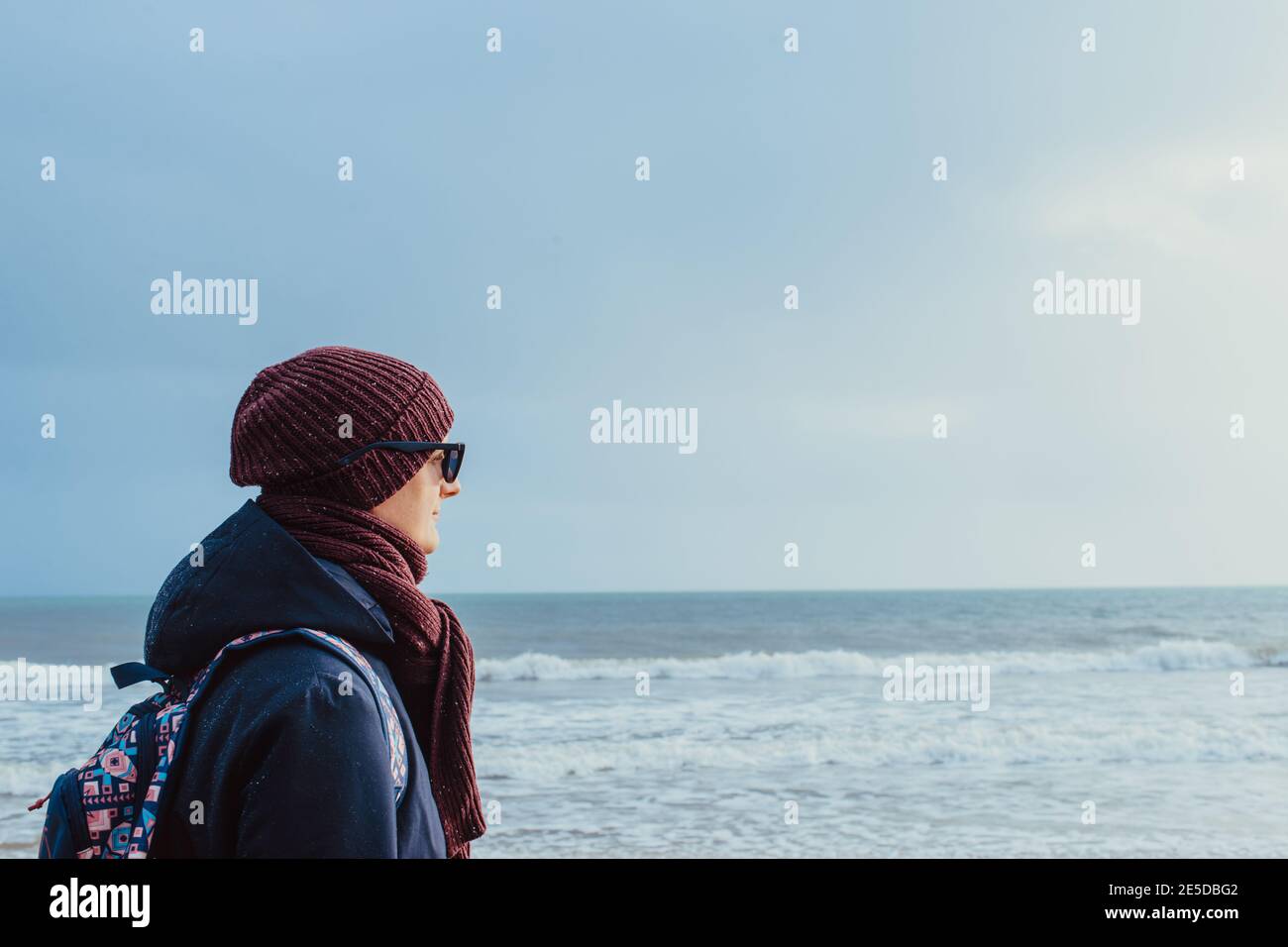 Un giovane in abiti caldi e occhiali da sole che cammina sul mare d'inverno e si gode il momento. Rilassati durante una passeggiata sulla costa. Locale che viaggia da soli Foto Stock