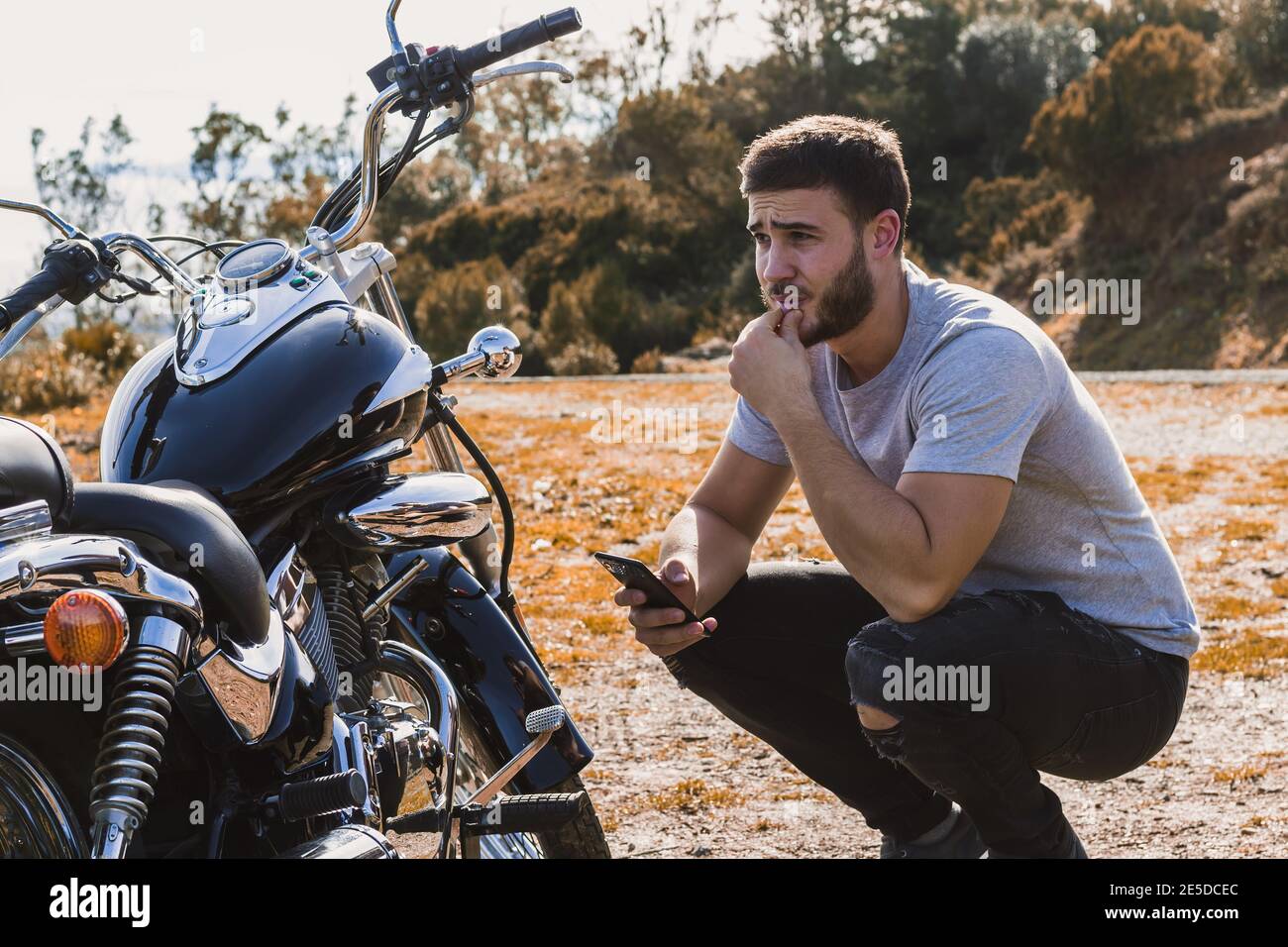 Motociclista accovacciato preoccupato per un guasto della motocicletta Foto Stock