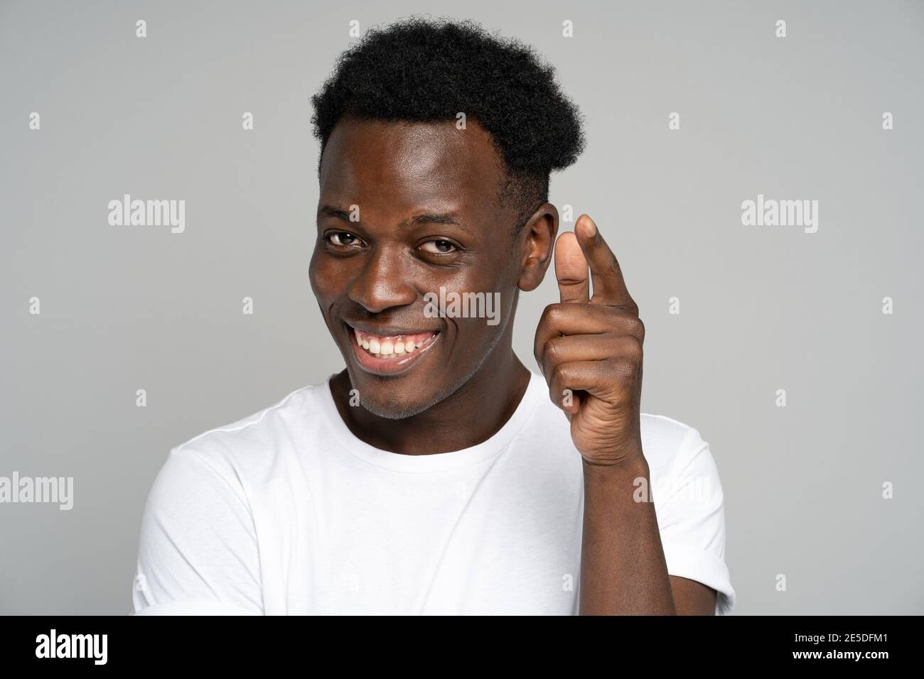 Allegro positivo afro hipster uomo sorridente ampiamente, puntando un dito verso di voi, studio sfondo grigio Foto Stock