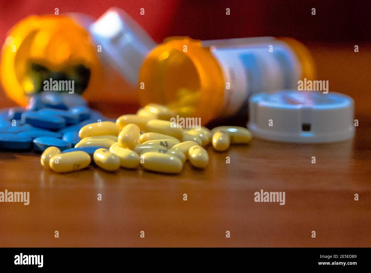 Giallo e blu pillole su una tabella con la prescrizione ribaltata bottiglie al di fuori della messa a fuoco e uno sfondo rosso Foto Stock