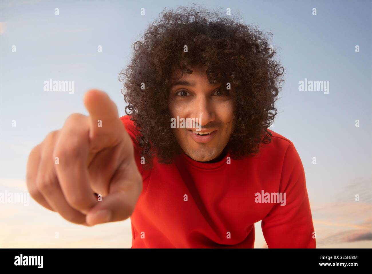 UN GIOVANE CON CAPELLI RICCI CHE PUNTA FELICEMENTE IL DITO VERSO FOTOCAMERA Foto Stock