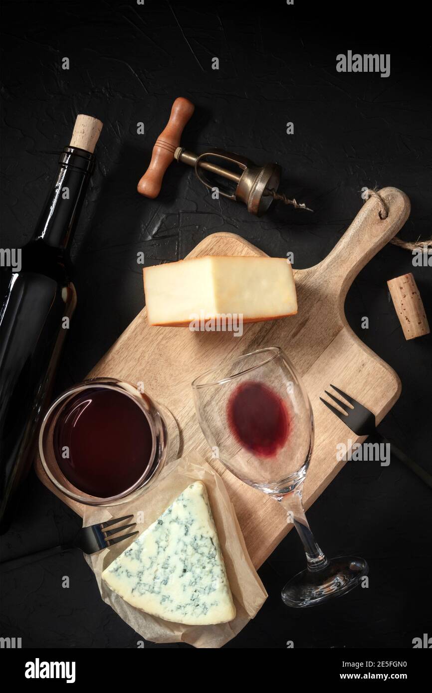 Degustazione di vini e formaggi, sparati dall'alto su sfondo nero, con cavatappi vintage e una bottiglia Foto Stock