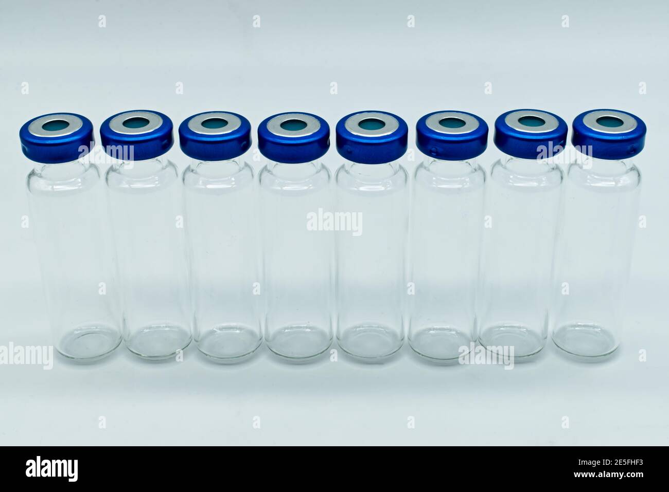 Fila di flaconcini medici in vetro trasparente per iniezione con coperchi sigillati blu, isolati su sfondo bianco. Foto Stock