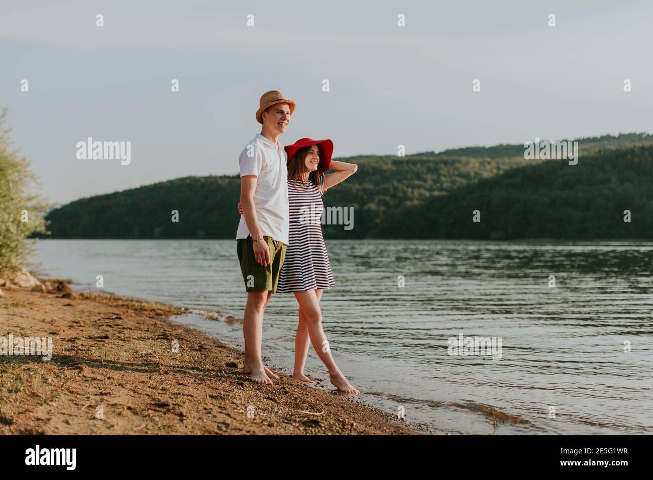 Tutta la coppia in amore rilassarsi sulla spiaggia in bella serata estiva. Ritratto di giovane donna e uomo che abbracciano al lago al tramonto. Foto Stock