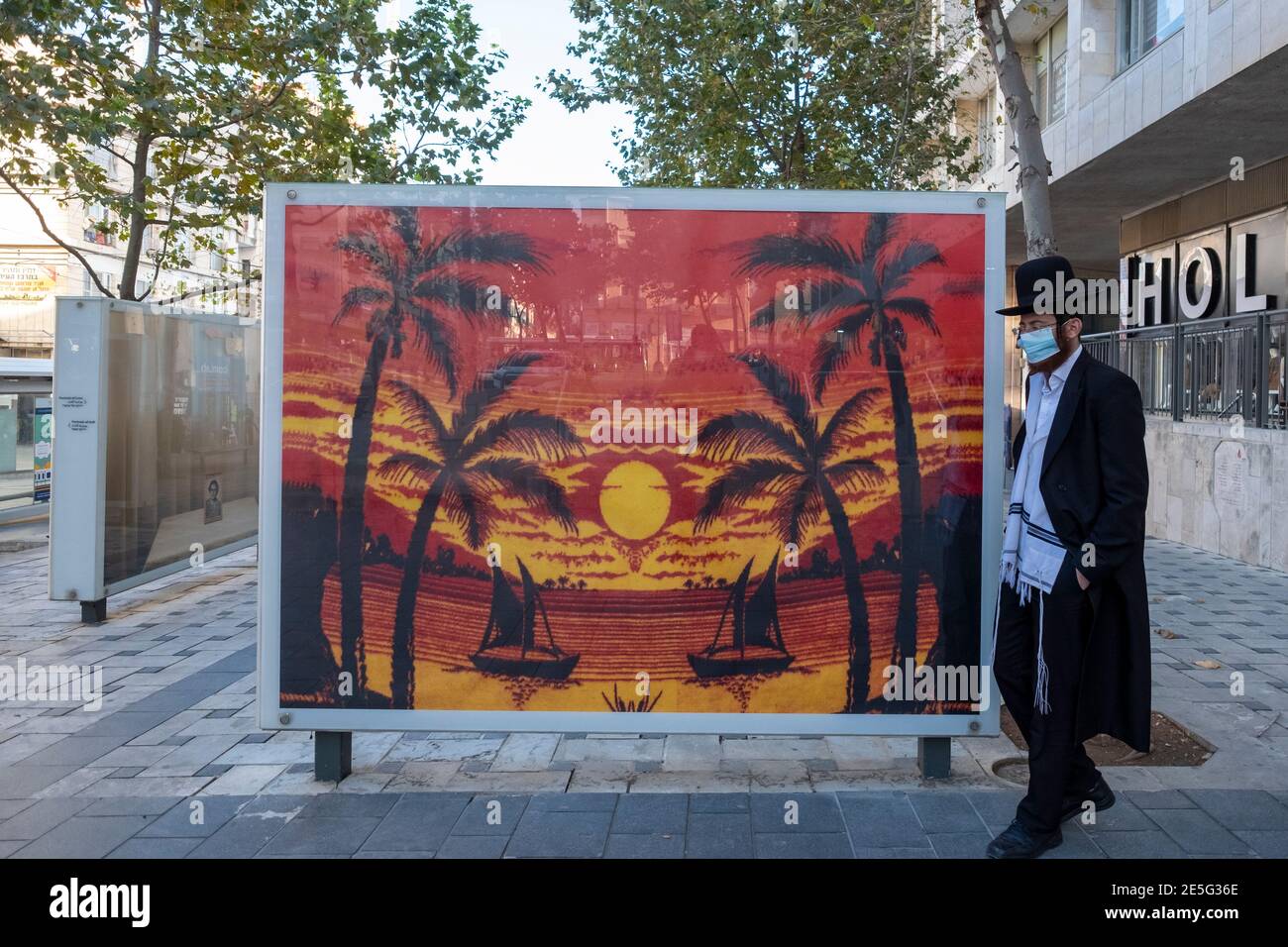 Un ebreo ultra ortodosso si trova accanto a un poster raffigurante Scena tropicale nel centro di Gerusalemme Ovest Israele Foto Stock