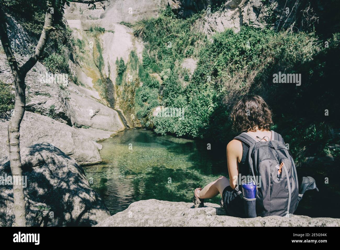 ragazza seduta su una roccia che guarda un paesaggio di una piccola cascata in una giornata di sole Foto Stock
