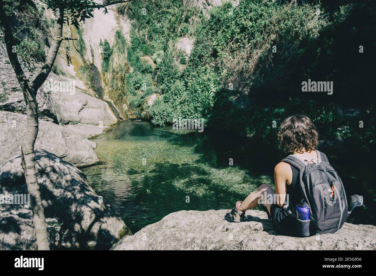 ragazza seduta su una roccia che guarda un paesaggio di una piccola cascata in una giornata di sole Foto Stock