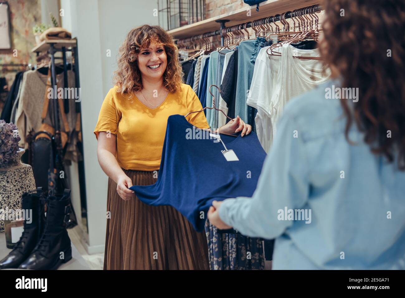 L'impiegato del negozio di moda aiuta il cliente femminile nella scelta dei vestiti in negozio. Venditore che assiste il cliente nel negozio di abbigliamento. Foto Stock