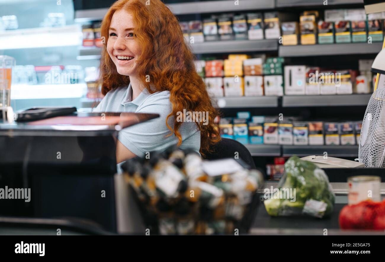 Felice cassiere donna che assiste il cliente al supermercato. Donna che lavora al negozio di alimentari checkout. Foto Stock