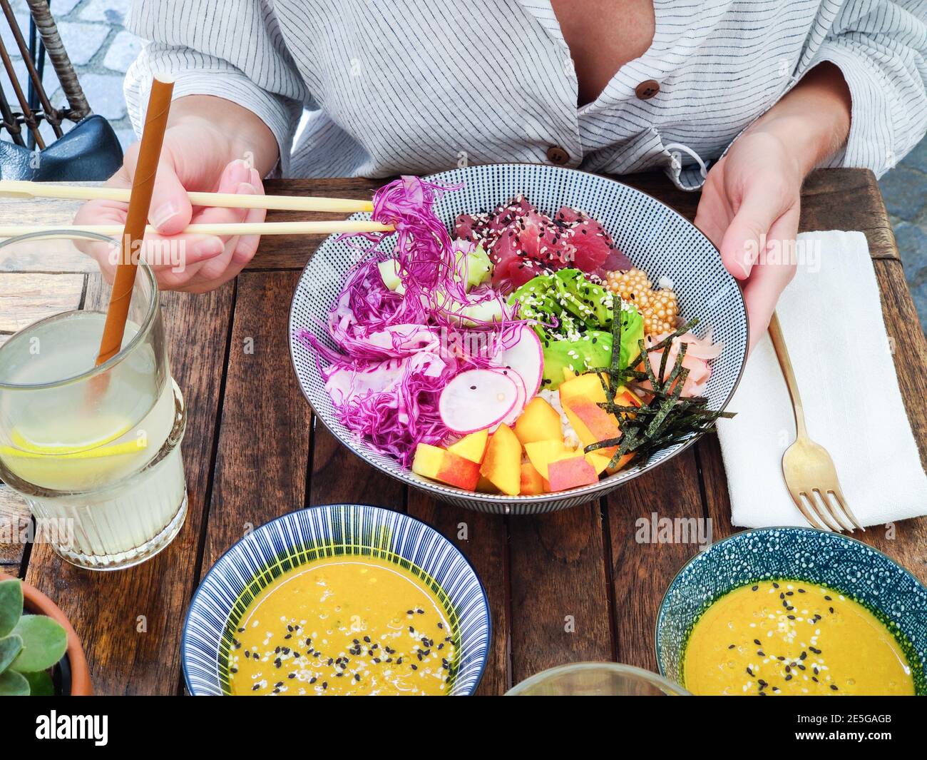 Donna che mangia gustoso colorato sano naturale vegetariano Hawaiiano poke ciotola utilizzando chopsticks asiatici su rustico tavolo di legno. Naturale sano Foto Stock