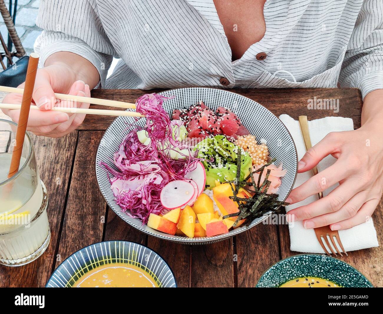 Donna che mangia gustoso colorato sano naturale vegetariano Hawaiiano poke ciotola utilizzando chopsticks asiatici su rustico tavolo di legno. Naturale sano Foto Stock